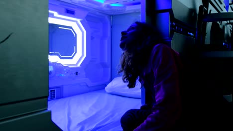Woman-looks-with-surprise-at-the-Sleepbox-with-neon-lights,-the-space-capsule-container-for-sleeping-at-the-airport