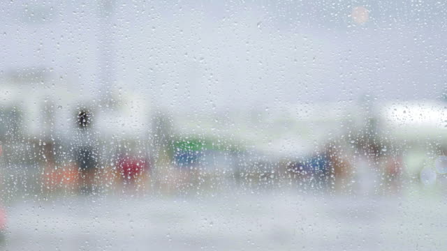 Raindrops-fall-on-airport-window-as-planes-bus-past