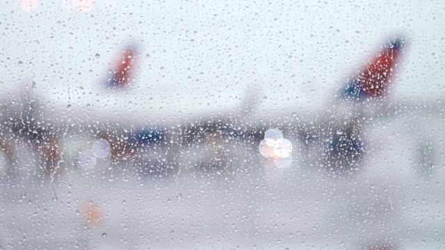 Raindrops-fall-on-bright-window-as-airplane-taxis-along-tarmac-on-rainy-day
