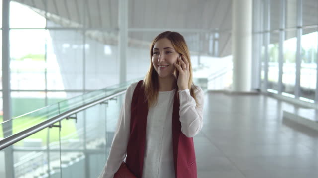 Positive-junge-Frau-in-eleganter-Kleidung-spricht-auf-Smartphone-beim-Einsteigen-auf-Flugzeug-auf-dem-Flughafen