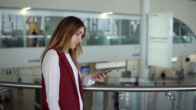 young-girl-in-elegant-clothes-stands-and-typing-in-the-smartphone-in-the-airport