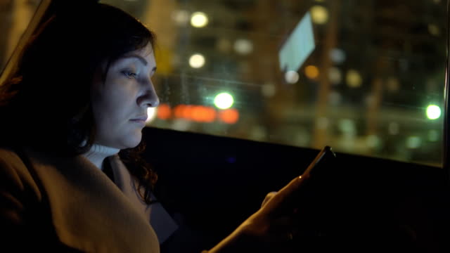 Mujer-joven-en-el-asiento-del-copiloto-de-un-coche-con-un-teléfono-con-paseos-por-la-ciudad-de-noche