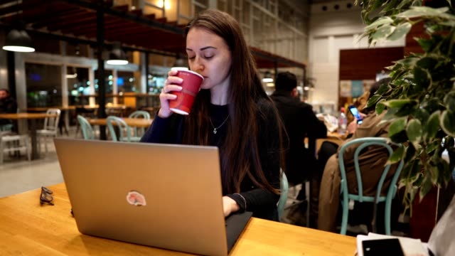 Young,-beautiful-girl-working-with-laptop-and-drinking-coffee-at-a-wooden-table