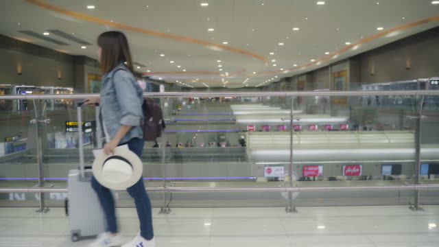 Happy-Asian-woman-using-trolley-or-cart-with-many-luggage-walking-in-terminal-hall-while-going-to-boarding-flight-at-the-departure-gate-in-international-airport.-Women-happy-in-the-airport-concept.