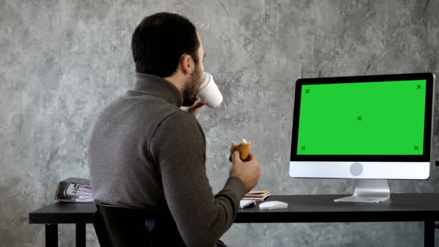 Business-Mann-im-Büro-Ihr-Frühstück,-Mittag--und-gerade-etwas-auf-dem-Mac-Computer.-Green-Screen-Mock-up-Display