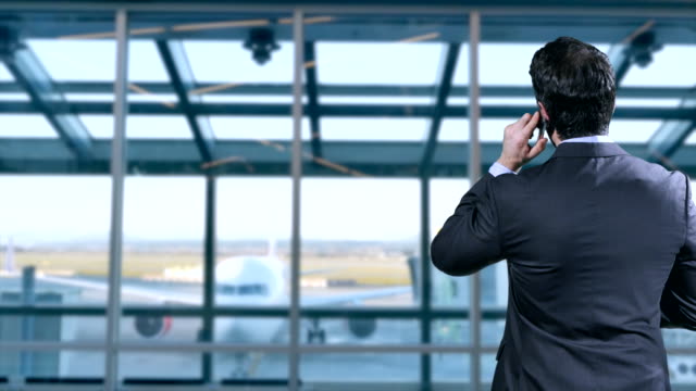 Mann-in-Anzug-spricht-auf-dem-Handy-als-Flugzeug-Taxis-in-Richtung-Terminal-Gate
