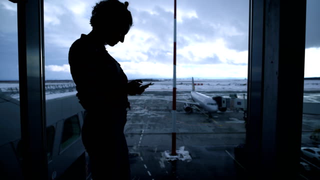 Silhouette-von-Fit-Mädchen-stand-in-der-Nähe-Flughafen-Fenster-und-mit-ihrem-Smartphone.-Formschöne-junge-Geschäftsfrau-warten-auf-ihre-Pension-nahe-dem-Tor-mit-dem-Fenster-und-Flugzeug-im-Hintergrund