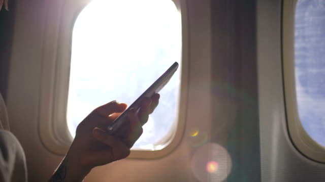 Nahaufnahme-der-Frau-die-Hände-sitzen-in-der-Nähe-von-Flugzeugfenster-mit-Handy-während-des-Fluges