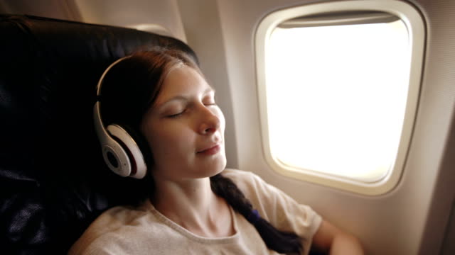 Junge-Frau-in-drahtlosen-Kopfhörern-Musik-hören-und-lächelnd,-während-im-Flugzeug-fliegen