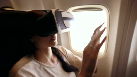 Mujer-joven-turista-relajarse-y-utilizar-auricular-VR-para-smartphone-durante-el-vuelo-en-avión