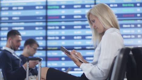 Mujer-de-negocios-adultos-atractivos-usando-tableta-mientras-espera-el-embarque-en-la-sala-de-embarque-en-el-aeropuerto.