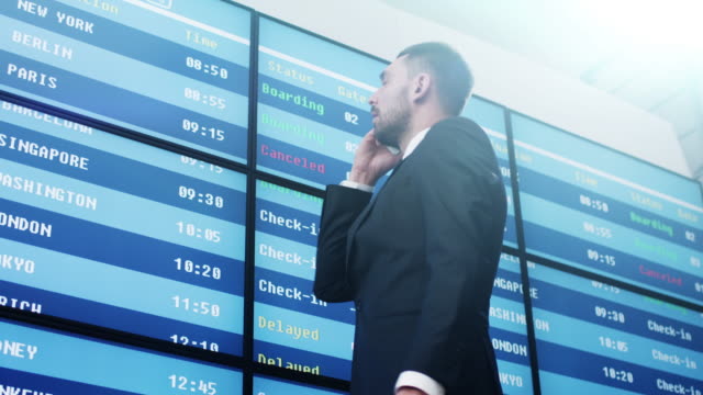 Businessman-talking-on-Mobile-Phone-while-Looking-at-Information-Board-at-the-Airport.