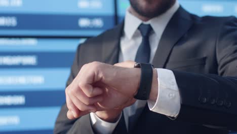 Geschäftsmann-sucht-Smart-Watch-stehen-neben-Infotafel-am-Flughafen.
