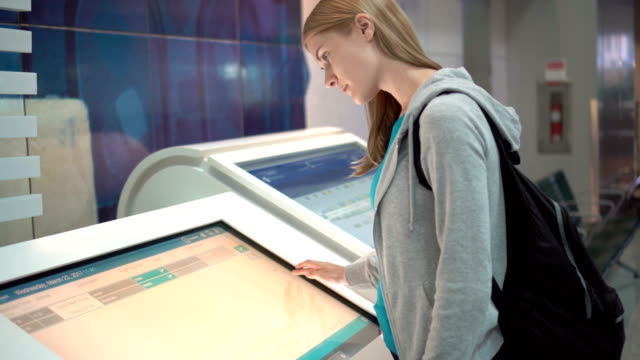 Beautiful-attractive-woman-in-airport-terminal.-Using-touchscreen,-searching-for-flight-information