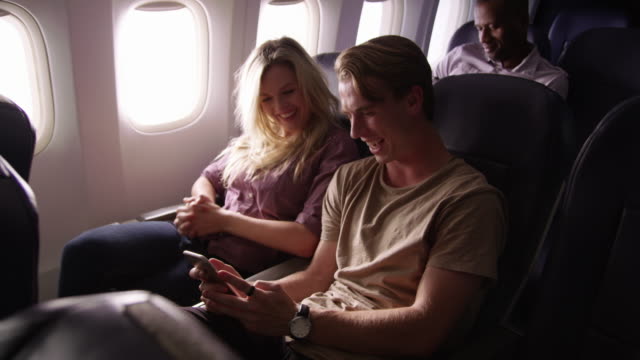 Couple-looking-at-mobile-phone-together-on-airplane-flight