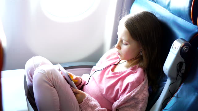 Entzückende-kleine-Mädchen-mit-dem-Flugzeug-reisen.-Süßes-Kind-mit-Laptop-in-der-Nähe-von-Fenster-im-Flugzeug