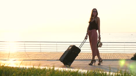 Señora-joven-con-maleta-en-la-playa-durante-la-puesta-de-sol,-dolly