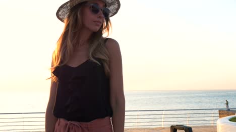 Junge-Geschäftsfrau-mit-Koffer-Hut-aufsetzen-am-Meer