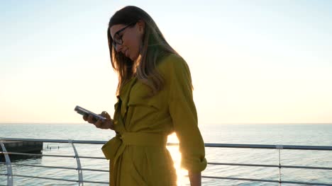 Señora-joven-con-maleta-con-smartphone-en-el-paseo-marítimo