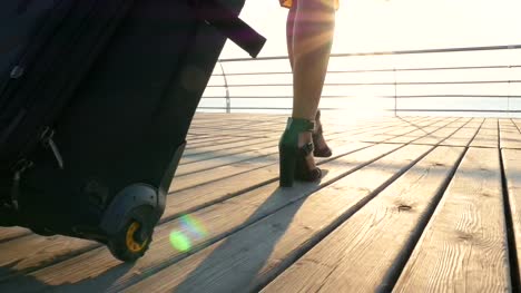 Young-business-lady-walking-with-suitcase-at-the-seafront-at-sunrise,-close-up