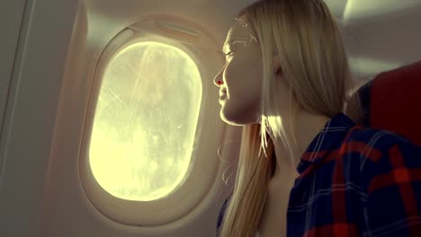 Auf-ein-Flugzeug-schöne-Blonde-Mädchen-sieht-aus-dem-Fenster.-Sonne-ist-Shining-auf-ihr-und-sie-lächelt.
