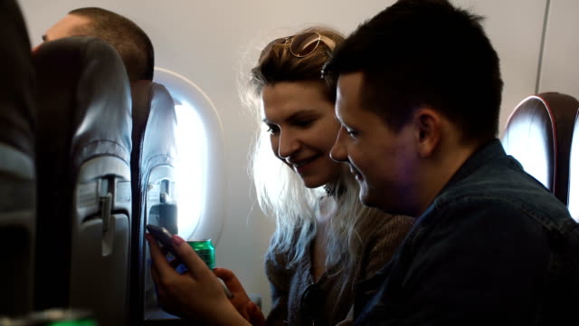 Junge-Brautpaar-sitzen-im-Flugzeug-in-der-Nähe-der-Fenster-und-mit-Smartphone.-Mann-und-Frau,-die-mit-dem-Flugzeug-reisen
