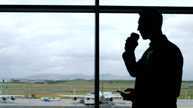 Hombre-de-negocios-tomando-café-y-sosteniendo-el-teléfono-móvil-en-el-aeropuerto