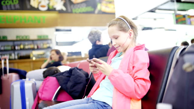 Kleine-Mädchen-spielen-auf-Smartphone-in-Flughafenhalle