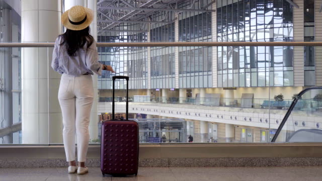 Young-woman-in-hat-with-baggage-in-international-airport-walking-with-her-luggage.-Airline-passenger-in-an-airport-lounge-waiting-for-flight-aircraft