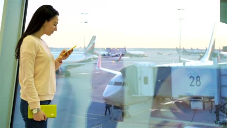 Porträt-der-jungen-Frau-mit-Smartphone-im-internationalen-Flughafen.-Flugreisenden-in-einer-Flughafenlounge-wartet-auf-Flug-Flugzeug