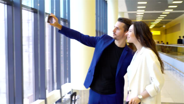 Couple-with-baggage-in-international-airport.-Man-and-woman-taking-selfie-near-big-window-in-aeroport