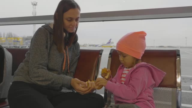 Mother-and-daughter-at-airport.-Little-girl-cleans-mandarin-at-waiting-hall.