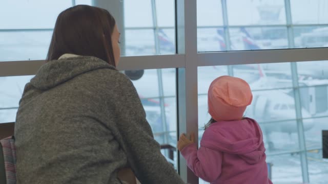 Junge-Mutter-und-Töchterchen-blickt-aus-Fenster-am-Flughafen