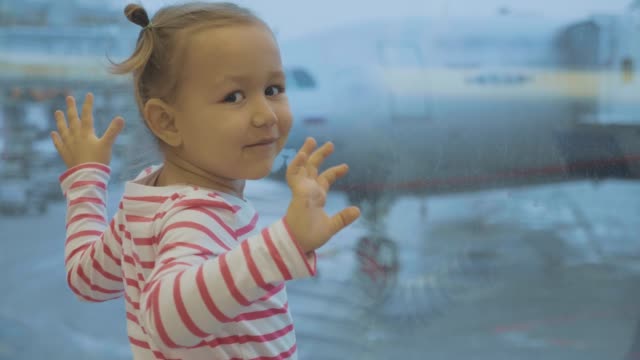 Kleines-Mädchen-steht-neben-Fenster-am-Flughafen-und-Wellen-in-Kamera