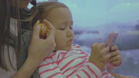 Mother-feeds-her-little-daughter-with-tangerine-at-airport-in-slow-motion