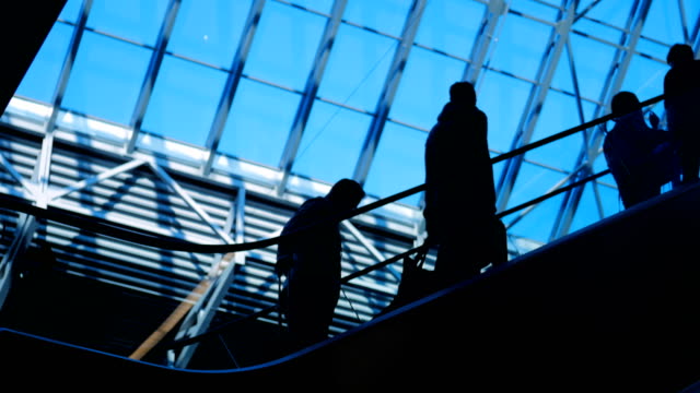 People-silhouettes-on-escalator-moving-in-shopping-center-with-large-windows