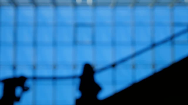 Blur-people-silhouettes-on-escalator-moving-inside-of-airport-with-large-windows