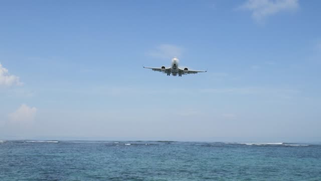 Airplane-landing-on-island-Bali-airport-under-blue-sea-with-waves-on-the-horizon