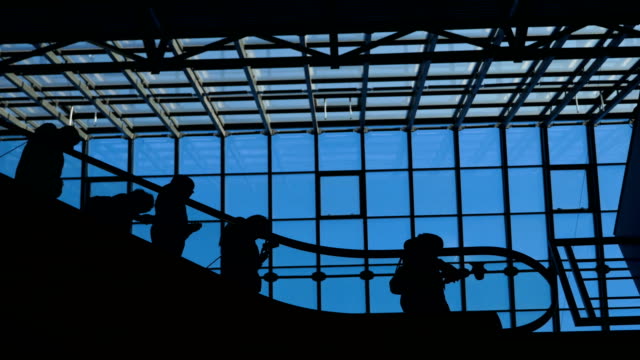 La-ecsalator-de-aeropuerto-de-ventana-de-vidrio-con-silueta-de-personas-en-movimiento