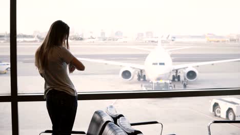 Young-European-businesswoman-stands-looking-from-airport-terminal-lounge-window,-looks-at-and-uses-smart-watch