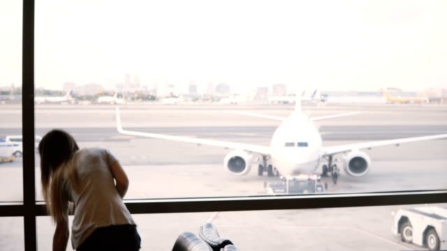 Bella-turista-está-parado-en-la-ventana-de-terminal-del-salón-de-aeropuerto-mirando-aviones,-luego-toma-la-bolsa-y-deja
