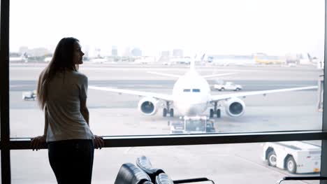 Kaukasische-Reisende-zu-Fuß-bis-zu-Flughafen-Lounge-terminal-Fenster,-Tasche-absetzen-und-mit-Blick-auf-smart-watch
