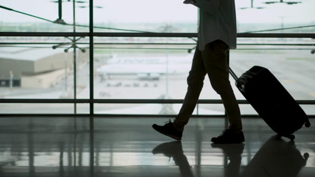 Pasajero-joven-macho-caminando-con-el-equipaje-de-la-maleta-en-el-área-de-salida-de-la-terminal-del-aeropuerto.-Empresario-asiático-en-ropa-casual-en-viaje-de-negocios.-Viajes-modernos-conceptos-de-estilo-de-vida.