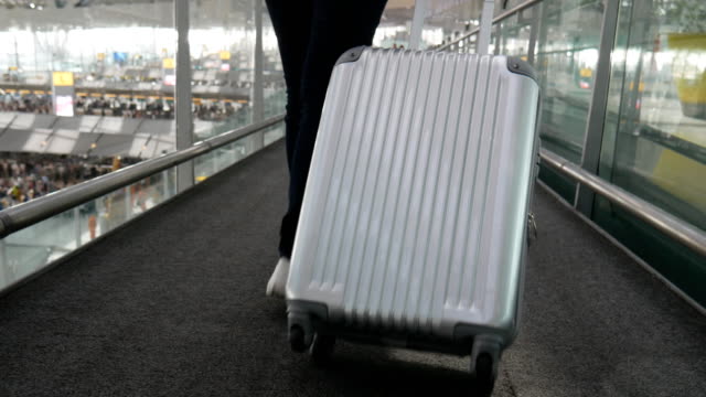 Close-up-of-woman-walking-with-trolley-suitcase-at-airport.-People-and-lifestyles-concept.-Back-view-and-low-angle