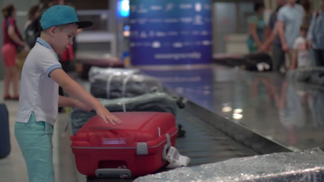 Boy-looking-for-his-suitcase-on-baggage-conveyor-belt-at-the-airport