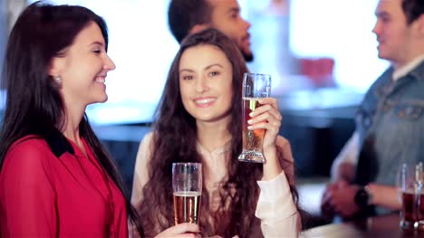 Two-cute-girls-standing-at-the-bar-are-talking-and-smiling-at-the-camera