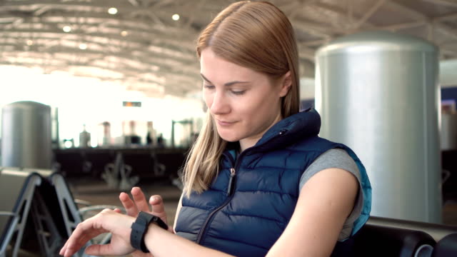 Schöne-Frau-mit-Smartwatch-im-Flughafen.-Surfen-Internet,-kommunizieren-mit-ihren-Freunden