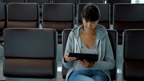 Mujer-que-usa-una-tableta-digital-en-la-zona-de-espera-del-aeropuerto