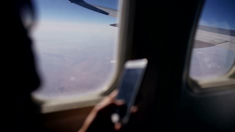 Nahaufnahme-der-Frau-die-Hände-sitzen-in-der-Nähe-von-Flugzeugfenster-mit-Handy-während-des-Fluges