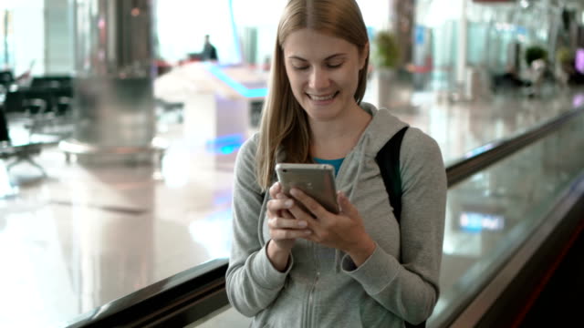 Woman-using-travolator-in-airport-terminal.-Waiting-for-flight.-Using-her-smartphone,-browsing